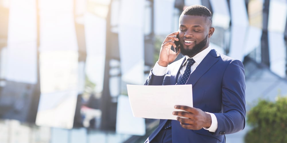 Man outside on his phone in a suit holding a piece of paper
